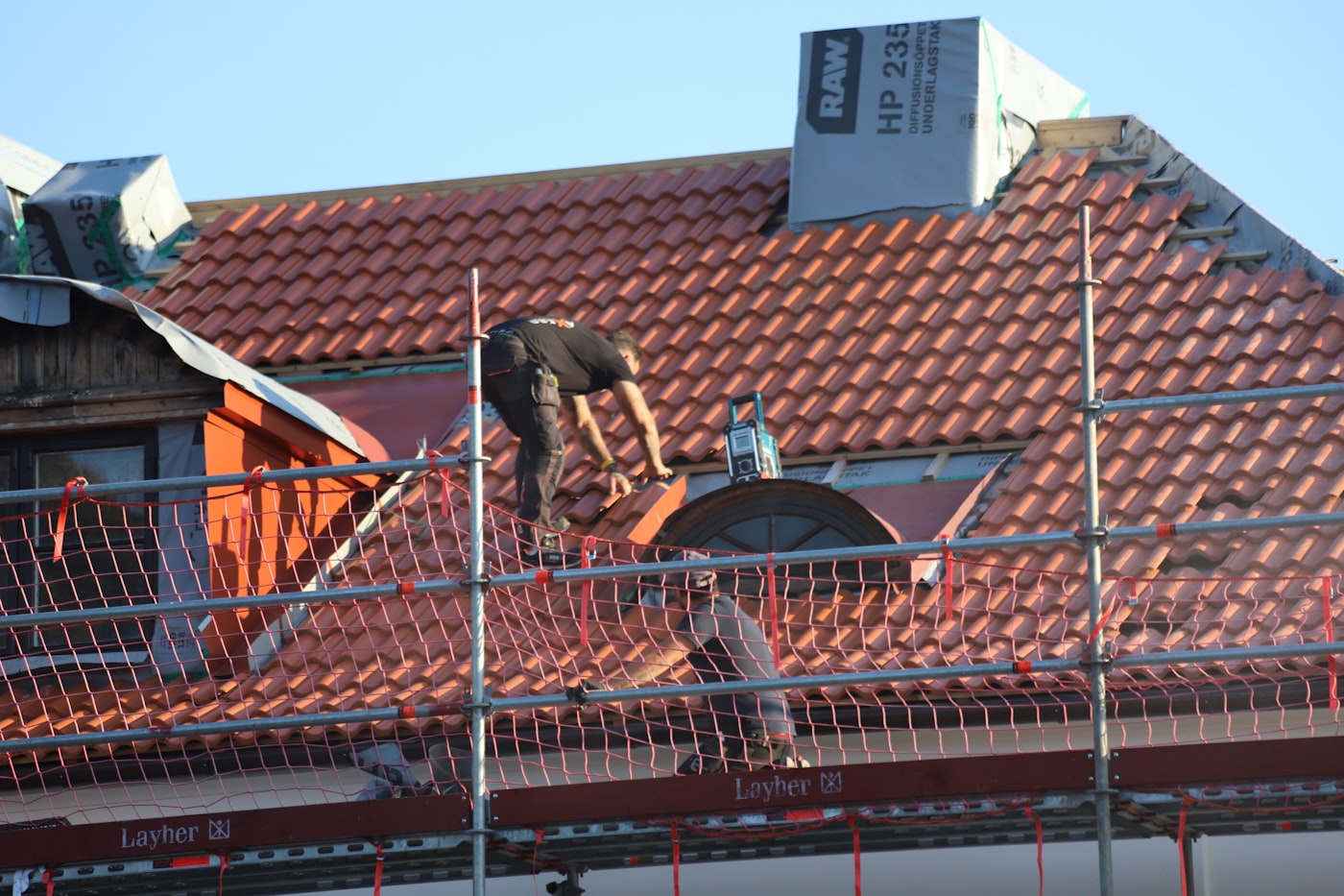 Roofer laying red clay tiles from scaffolding
