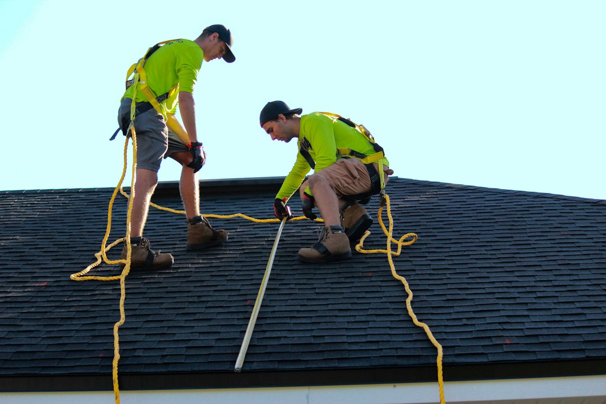 Two roofers in safety harnesses inspecting a shingle roof