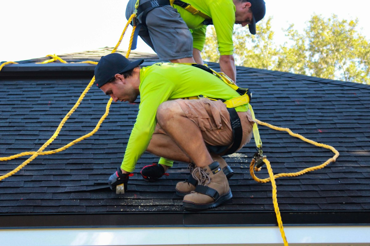 Roofer fastening shingles with a power drill