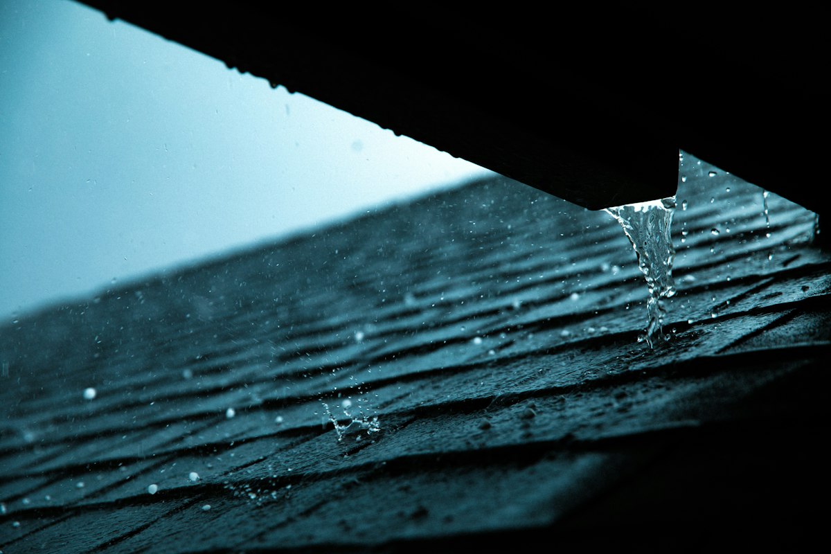 Rainwater spilling over a roof edge during a storm