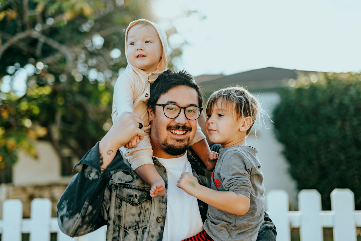 Smiling father carrying his two children outside their home